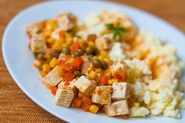 Healthy vegetarian cuisine with tofu with colorful roast vegetables including carrot, peas and maize served with mashed potatoes. Selective focus