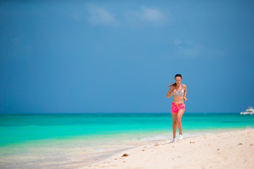 Fototapeta na wymiar Fit sports young woman running along tropical beach in her sportswear 