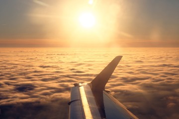 Plane wing and sun over the clouds