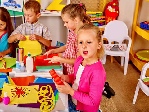 Group children holding colored paper on table in kindergarten . Child development.