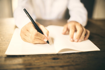 Man writing with pen in blank notebook on wooden table