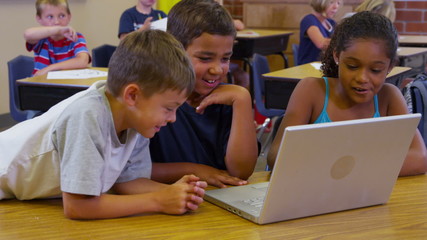 Three elementary school students look at laptop computer together - Powered by Adobe