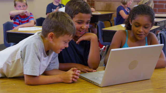 Three elementary school students look at laptop computer together