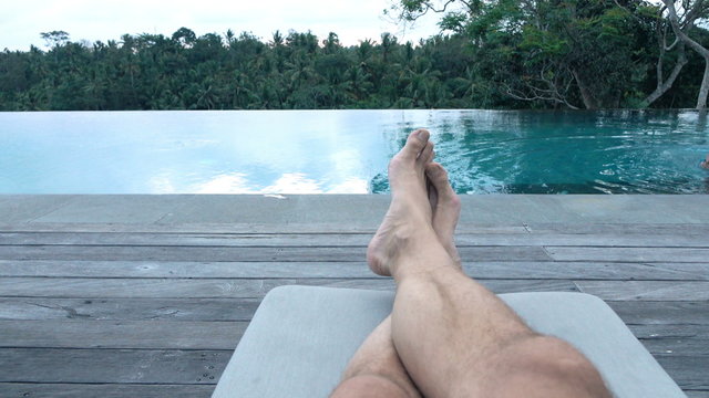 Male legs on daybed by the swimming pool
