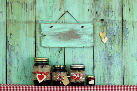 Blank mint green sign hanging by gold hearts over jars of fruit jam 