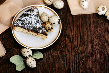 Piece of cake and quail eggs on a wooden background.