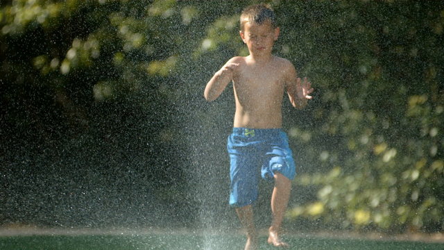 Kid jumping over sprinkler, slow motion