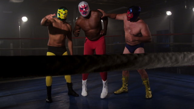 Three masked wrestlers stand in ring