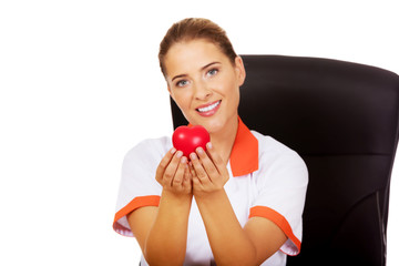 Female doctor  sitting behind the desk and holding heart toy