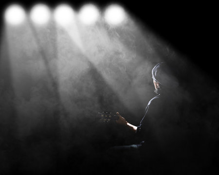 Man playing guitar with spotlight and smoke.