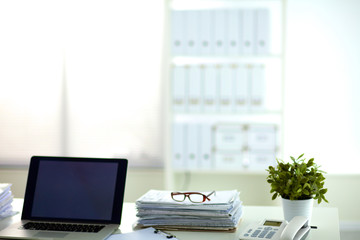 Laptop with stack of folders on table on white background