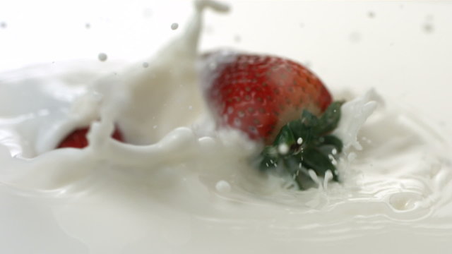 Fresh strawberries splashing into cream, slow motion