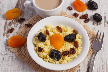 Cooked millet groats on white plate and cup of coffee with milk, healthy food and nutrition