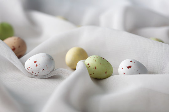 Chocolate speckled Easter eggs in crisp sugar shell among delicate white gauze fabric folds that looks like milk. Shallow depth of field.