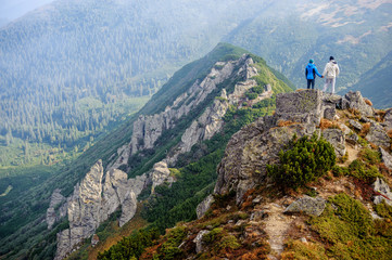 Backpackers couple standing on rocky mountain summit, holding hands and enjoying the view on beautiful valley.