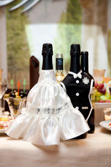 Two bottles of champagne in bride and groom clothes on restaurant table