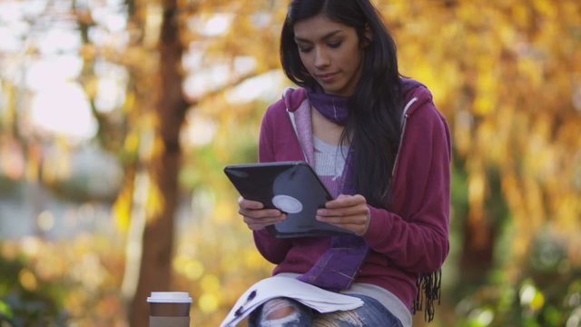 College student using digital tablet outdoors in autumn