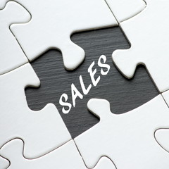 Blank white jigsaw puzzle with a missing piece revealing the word Sales in white text on black