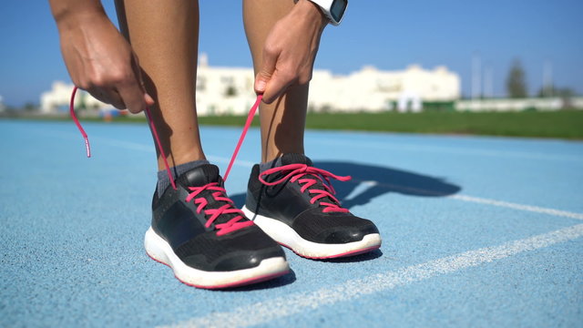 Runner woman tying the laces of her running shoes getting ready for race on run track. Female athlete preparing for cardio training .Closeup of feet and hands.