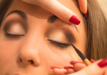 Applying makeup, eyeliner on a beautiful age-related woman face.