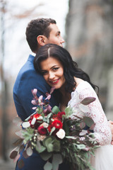 Gorgeous wedding couple kissing and hugging in forest with big rocks