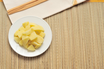 patate tagliate, crude, in un piatto bianco su una tovaglietta di bambù, vista dall'alto, luce del sole