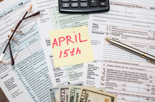 1040 tax form with sticky note of april 15, us dollar  and calculator