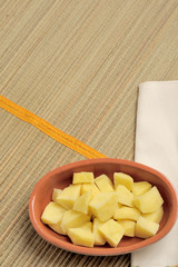 mucchio di patate a cubetti in una ciotola di coccio, su una tovaglietta di bambù, verticale con spazio per testo