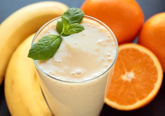 Glass with healthy smoothie with banana and oranges decorated with fresh mint leafs