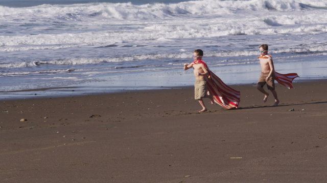 Two young boys running at beach with superhero costumes
