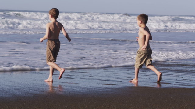 Two boys running in ocean together, slow motion
