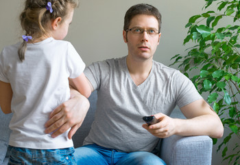 Little girl disturbing her dad while he is watching TV.