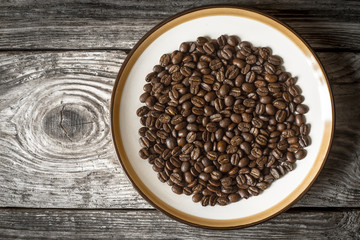 Fototapeta premium Coffee beans on the plate on the wooden table top view