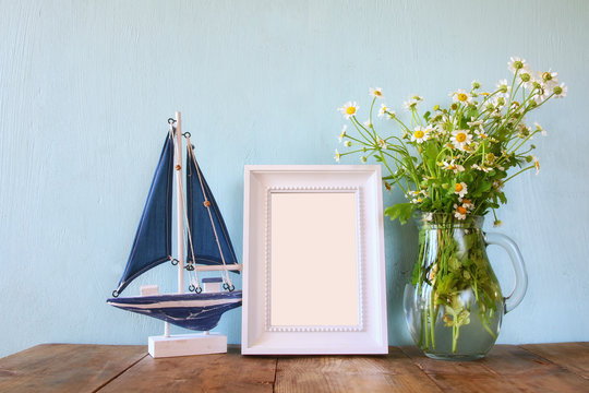fresh daisy flowers, blank photo frame and wooden boat on wooden table
