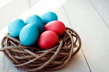 Multicolored Easter eggs in wicker basket on white wooden background