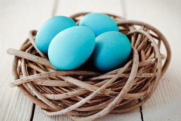 Multicolored Easter eggs in wicker basket on white wooden background