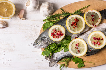 Fototapeta na wymiar Fish dish cooking with various ingredients. Raw rainbow trout with lemon, garlic ,herbs and spices on cutting board , top view. Healthy food or diet nutrition concept.