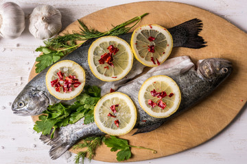 Fish dish cooking with various ingredients. Raw rainbow trout with lemon, garlic ,herbs and spices on cutting board , top view. Healthy food or diet nutrition concept.