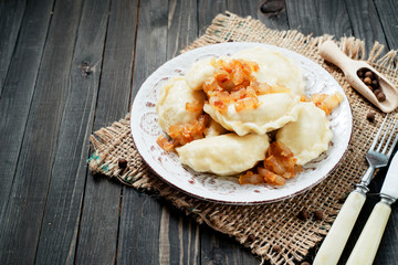 traditional Ukrainian and Russian cuisine , dumplings called varenyky of dough with meat, pepper and fat or salo in a clay plate on a dark wooden background