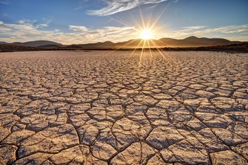 Sunrise over cracked earth in a barren landscape with a mountain backdrop, Fossil Falls National Historic Site, Mojave Desert, California, USA