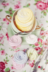 Small spiral meringues  on the tablecloth with a floral pattern. Toned image. Pastel colored. Top view