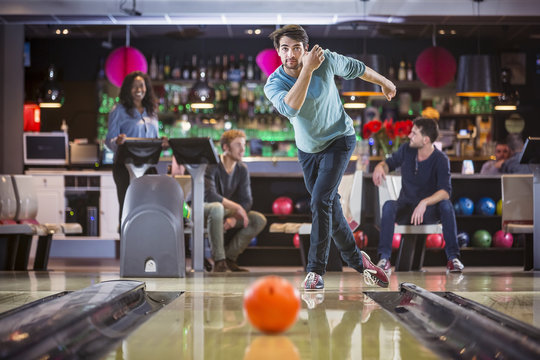 Young man is bowling with his friends, looking concentrated