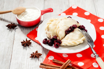 traditional Ukrainian and Russian cuisine , sweet dumplings called varenyky of dough with cherry, sour cream and cinnamon in a clay plate on a white wooden background