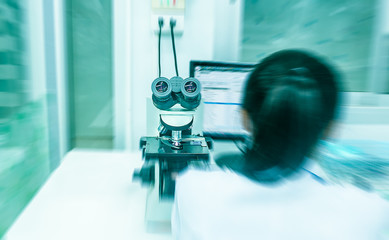 women with blue blur background and red ray use microscope for find microscopic organism on the table