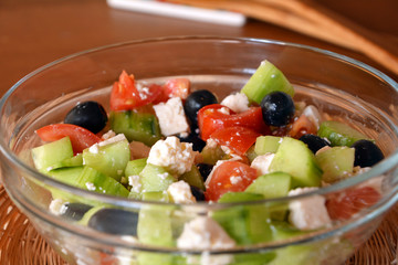 Fresh mixed vegetable salad with pieces of cheese on a glass bowl