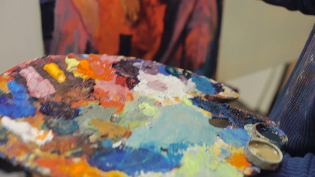 artist brush mix color oil painting on palette is holding in his hand closeup