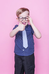 Little adorable boy in tie and glasses. School. Fashion. Studio portrait over pink background