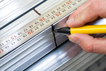 Hand holding marker pen marking measurement on a metal stud