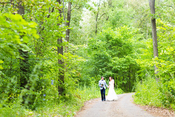 Fototapeta premium Bride and groom at wedding Day walking Outdoors on spring nature. Happy Newlywed embracing in green park. 