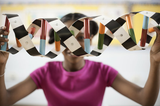 A girl in a science class holding a model of a helix structure in front of her face,